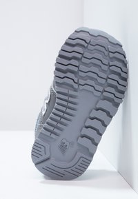 Szara podeszwa z sneakersów z teksturowanego, grubego materiału gumowego. Posiada głębokie bieżniki oraz gładki, zaokrąglony obcas z logo blisko dolnej części.