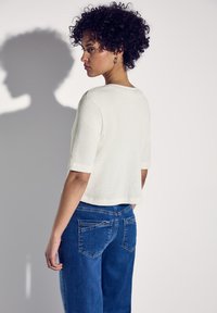 Krämfärgad tröja med korta ärmar, kombinerad med högmidjade blå denimjeans som har bakfickor och sömdetaljer.