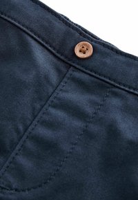 Tela de color azul marino con una textura suave y costuras visibles, con un botón de madera en la cintura. Vista en primer plano del área del bolsillo.