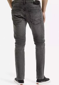 Szare dżinsy o dopasowanym kroju, z tylnymi kieszeniami i subtelną fakturą. W połączeniu z czarnymi trampkami, z białym logo.