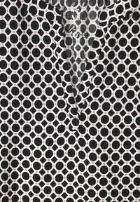 Czarno-biała tkanina z dużymi czarnymi kółkami i rombami, z małymi różowymi kropkami podkreślającymi wzór oraz dekoltem w kształcie litery V.