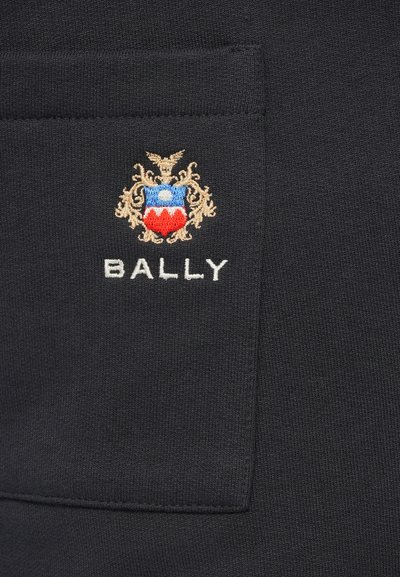 Crna tkanina s malim džepom na kojem je izvezena višebojna grb i tekst "BALLY" ispod grba.