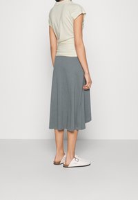 Light yellow, fitted short-sleeve top paired with a gray, knee-length, A-line skirt. Footwear is white clogs with a brown accent.