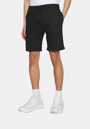 Shorts neri in cotone con vita elastica e cordino, dotati di un patch logo testurizzato sulla gamba sinistra. Abbinati a sneakers bianche.