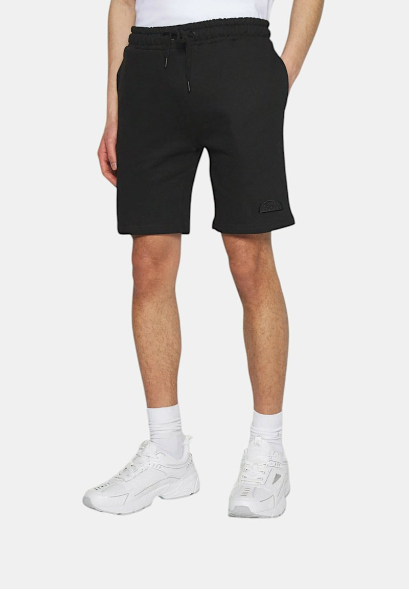 Shorts neri in cotone con vita elastica e cordino, dotati di un patch logo testurizzato sulla gamba sinistra. Abbinati a sneakers bianche.