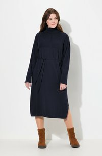 Tummansininen neulemekko, jossa on korkeakauluksellinen design, pitkät hihat ja vyötäröllä oleva vyö. Sisältää tekstuuripintoja ja sivureikiä. Yhdistetty ruskeisiin nilkkureihin.