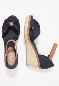 Sandales compensées bleu marine avec des brides de cheville couleur camel, des talons plateforme à texture de corde et un nœud en tissu sur la bride avant.