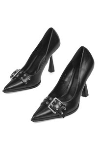 Zapatos de tacón alto de cuero negro con punta puntiaguda y una correa ancha con hebilla adornada con tachuelas plateadas en la parte frontal. Textura lisa, tacón afilado.