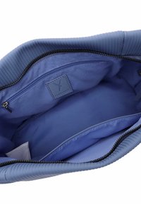 Blaues Textilinterieur einer Tasche mit einem Reißverschlussfach, das eine glatte Fütterung und ein Logo-Patch aufweist, wobei das strukturierte Design und subtile Akzente hervorgehoben werden.