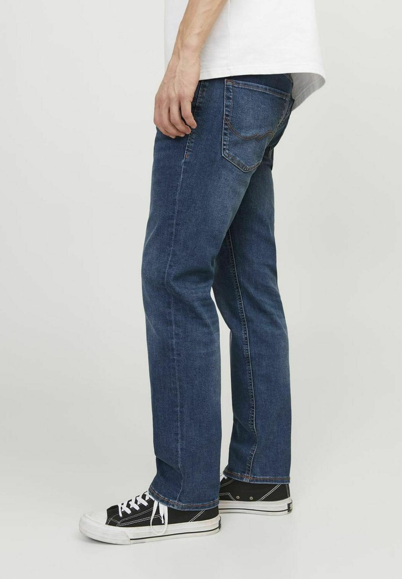 Jean en denim bleu avec une coupe droite, dotés de poches arrière et de détails de couture subtils. Portés avec des baskets noires à tige basse.