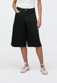 Μαύρα denim culottes με φαρδιά παντελόνα, διαθέτουν κούμπωμα με κουμπιά και πλαϊνές τσέπες. Συνδυάζονται με ροζ ανοιχτόχρωμα παπούτσια με κορδόνια.