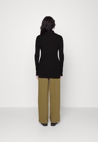 Svart långärmad tröja med hög krage, matchad med vida olivgröna byxor. Slät textur och minimalistiska design detaljer.