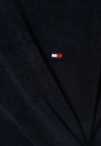 Námořnická modrá bavlněná koupací pláštěnka s jemnou texturou, na hrudi se nachází malé vyšívané logo v červené, bílé a modré barvě.