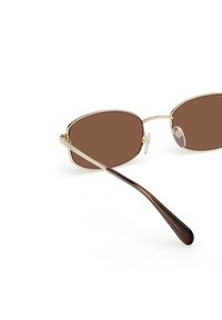 Occhiali da sole oversize con tonalità marrone, dotati di una sottile montatura in metallo dorato, con bordi curvi e aste marroni sfumate con una finitura lucida.