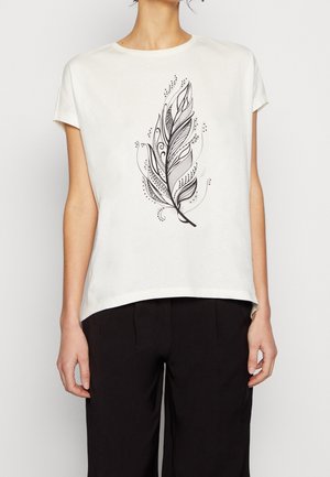 Mujer con camisa blanca de manga corta con un detallado diseño de plumas negras en el frente, combinada con pantalones negros.
