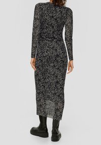 Langärmliges Kleid aus transparentem schwarzem Gewebe mit einem weißen abstrakten Muster, das eine taillierte Taille und einen knielangen Saum aufweist. Gemeinsam mit schwarzen Stiefeln.