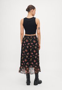 Svart crop top med ermene design, paret med et langt blomsterkjole med rosa og gule blomster og en gjennomsiktig volangkant. Sorte støvler.