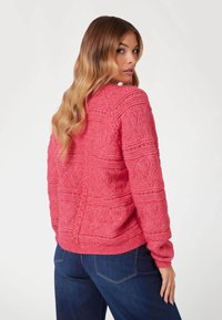 Maglione lavorato a maglia di un vivace colore rosa con motivo testurizzato e polsini a costine. Presenta una vestibilità leggermente oversize e un dettaglio della cucitura posteriore. Abbinato a jeans scuri.