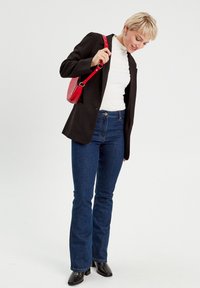 Schwarzer Blazer, weißer Rollkragenpullover, ausgestellte dunkelblaue Jeans und eine kleine rote Handtasche. Schwarze Stiefel mit Absatz ergänzen das Outfit. Schlichtes und modernes Design.