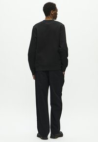 Black sweatshirt with a round neck and ribbed cuffs, paired with black wide-leg pants. Simple, solid design, textured fabric.