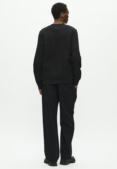 Schwarzer Sweater mit Rundhalsausschnitt und gerippten Bündchen, kombiniert mit schwarzen, weiten Hosen. Einfaches, schlichtes Design, strukturierter Stoff.