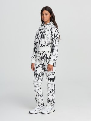 Set di felpa bianca con cappuccio e pantaloni, decorato con motivi grafici neri, che includono parole e icone. Il materiale sembra morbido; include un cappuccio con cordino.