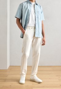 Ljusblå kortärmad denimskjorta över en vit t-shirt, kombinerad med off-white linnebyxor och vita sneakers. Avslappnad outfit.