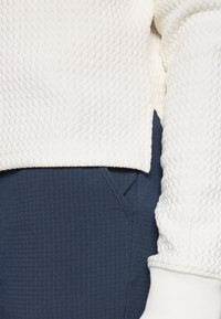Bela teksturirana sweatshirt s okruglim izrezom i tamnoplave hlače s suptilnim prugastim uzorkom i bočnim džepovima.