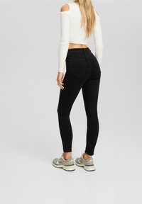 Los jeans ajustados de cintura alta negros presentan un diseño clásico de cinco bolsillos y una textura suave, combinados con una parte superior corta de manga larga blanca y acanalada.