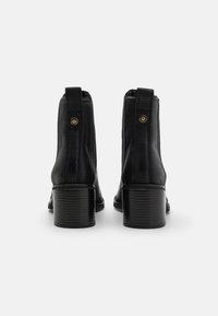 Botines de cuero negro con puntera redondeada, tiradores y tacón grueso texturizado. Acabado liso con detalles de costuras en contraste.