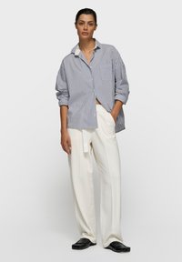 Chemise à rayures bleu et blanc à boutons, avec une poche poitrine, associée à un pantalon blanc ample et des chaussures noires. Texture de tissu lisse.