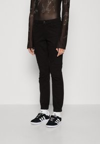 Svarta cargobyxor med slim fit, avsmalnande ben och flera fickor. Bärs med svarta mockaskor och vita strumpor. Transparent, långärmad topp.