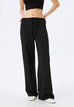 Schwarze weite Hose mit einem Kordelzugbund, hergestellt aus weichem, dehnbarem Material. Sie verfügt über einen lässigen Schnitt und eine glatte Textur.