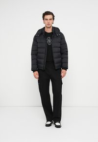 Μαύρο φουτερδάκι με αποσπώμενη κουκούλα, μπροστινό φερμουάρ και μπροστινές τσέπες, συνδυασμένο με ένα μαύρο μπλουζάκι με γραφικά και σκούρα cargo παντελόνια.