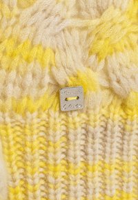 Indumento lavorato a maglia in filato crema e giallo, caratterizzato da un motivo testurizzato. Include un piccolo targa metallica con incisione "Manila Grace".