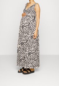 Maxi sukienka w beżowo-czarny wzór zebry, z dekoltem w kształcie litery V, bez rękawów i luźnym krojem. Połączona z czarnymi sandałami.