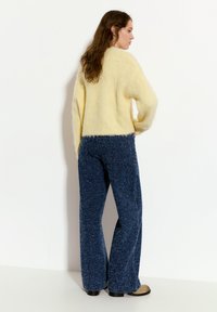 Hellgelbes, flauschiges Sweatshirt mit einem cropped Design, kombiniert mit marineblauen, weit geschnittenen Hosen. Die Hosen haben eine strukturierte Oberfläche und einen dezenten Glanz.