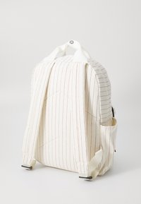 Rucsac matlasat în crem cu dungi roșii. Include bretele moi pentru umeri, un mâner de sus și un buzunar lateral pentru stocare. Material durabil.