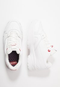 White leather sneakers with red accents, lace-up closure, perforated toe, padded collar, and textured rubber outsole.