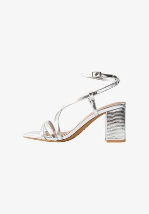 Srebrne metaliczne sandały na obcasie z kwadratowym noskiem, z krzyżującymi się paskami i zapięciem na kostkę. Block heel ma textured surface.
