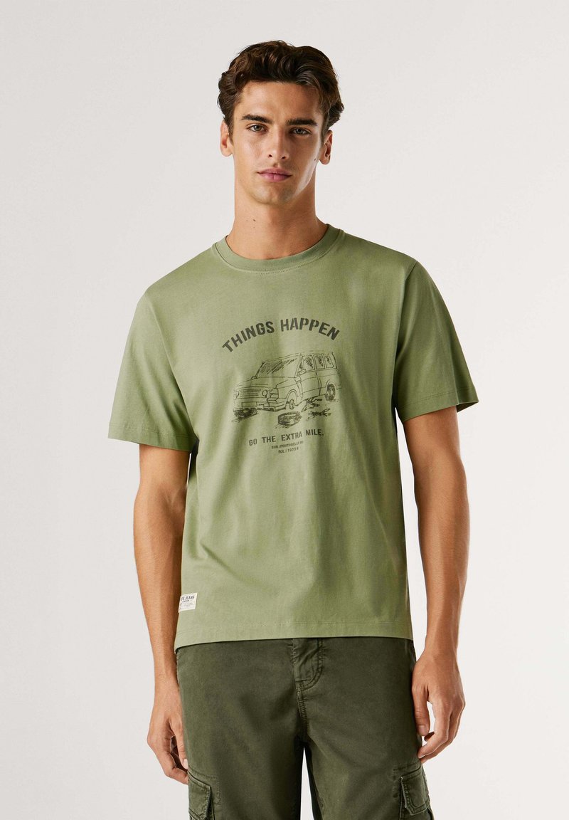 Camiseta de algodón verde oliva con mangas cortas, cuello redondo y gráfico impreso de una furgoneta con el texto "LAS COSAS SUCEDEN, VE UN PASO MÁS ALLÁ."
