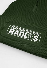 Dark green knitted beanie with ribbed texture and a rectangular white patch featuring the text “ICH BIN SELTEN RADLOS” and a bike icon.