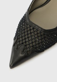 Schwarzer High-Heel-Schuh mit einem oberen Teil aus Netzstoff und einem Diamantmuster, spitz zulaufender Zehenpartie, Lederakzenten und transparenten Details entlang des Randes.