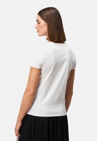 T-shirt blanc à manches courtes, design ajusté, en coton lisse, col rond, associé à une jupe plissée noire.