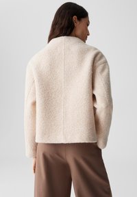 Giacca in misto lana di colore rosa chiaro, con un taglio corto, maniche ampie e colletto alto, caratterizzata da un design pulito e minimalista.