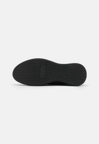 Suela de zapato de goma negra con un patrón texturizado de panal, que presenta un logotipo incrustado en una sección rectangular cerca del centro.