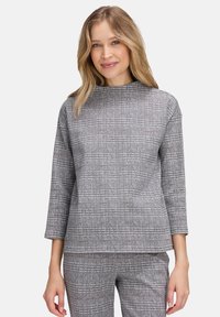 Haut à carreaux gris avec manches trois-quarts, col montant, tissu texturé et coupe décontractée. Remarquable pour ses accents bruns subtils dans le motif.