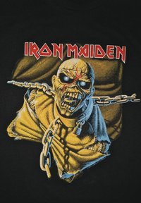 Černé tričko s grafikou postavy podobné zombie s řetězem, s živými žlutými a modrými barvami a textem "IRON MAIDEN" nahoře.