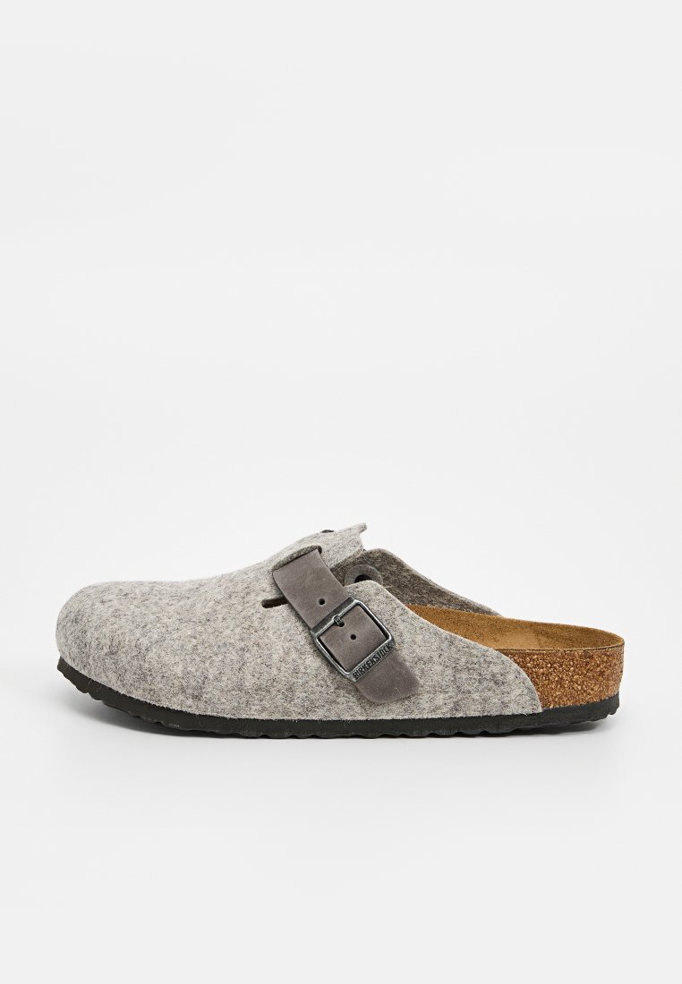 Grau gefütterter Clog mit braunem Korkfußbett, verstellbarem grauem Riemen mit metallischer Schnalle, abgerundeter Zehenpartie und strukturiertem schwarzen Gummisohle.