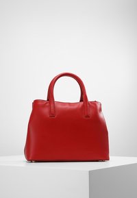 Sac à main en cuir rouge avec deux poignées courtes, un design structuré, une texture lisse et des accents matériels subtils à la base.